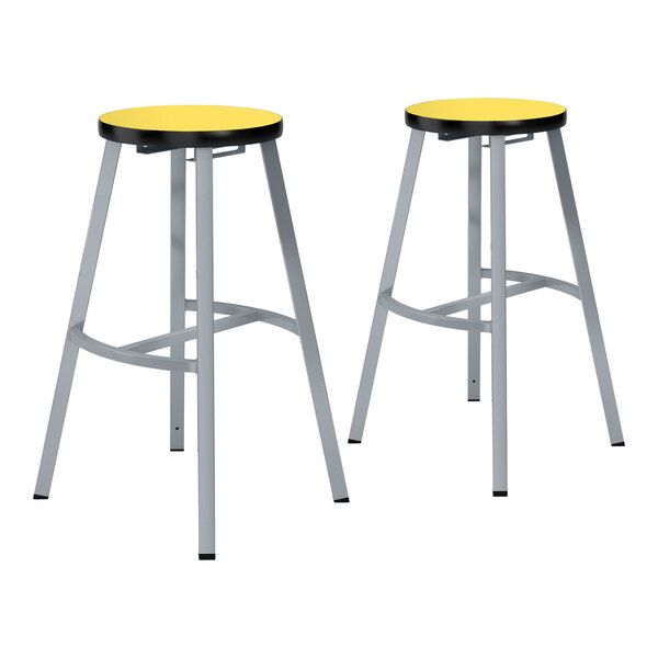 A pair of National Public Seating lab stools with marigold seats and black legs.