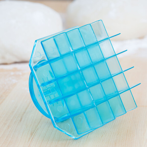 A blue plastic Mexican bread stamp with a waffle design on top of dough.