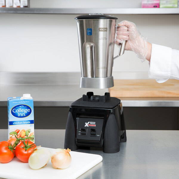 A person's gloved hand using a Waring commercial blender on a counter.