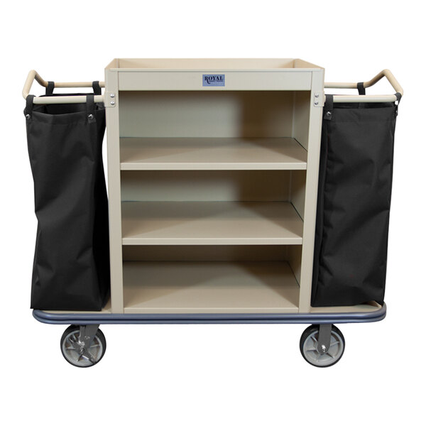 A beige Royal Basket Trucks housekeeping cart with black bags on the bottom shelf.