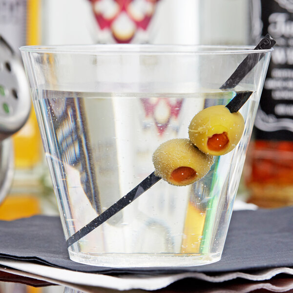 A close up of a Fineline clear plastic tumbler with a drink and olives in it.