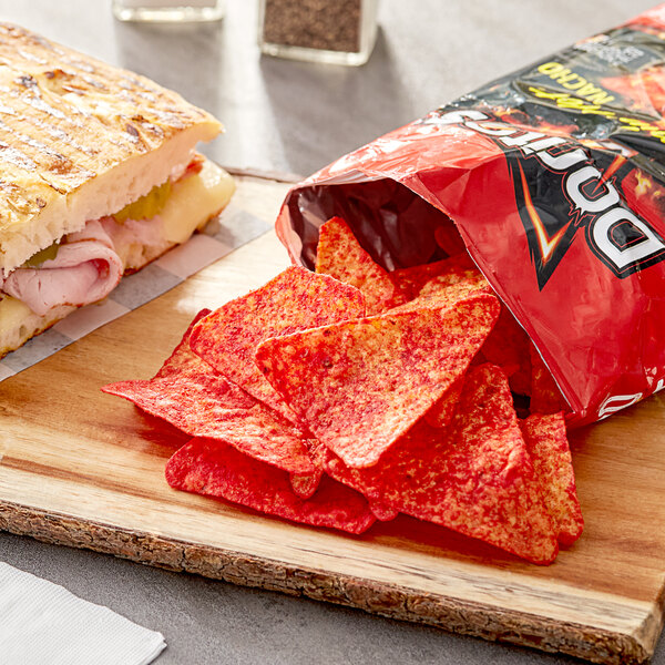 A sandwich and a bag of Doritos Flamin' Hot Nacho Cheese flavored tortilla chips on a cutting board.