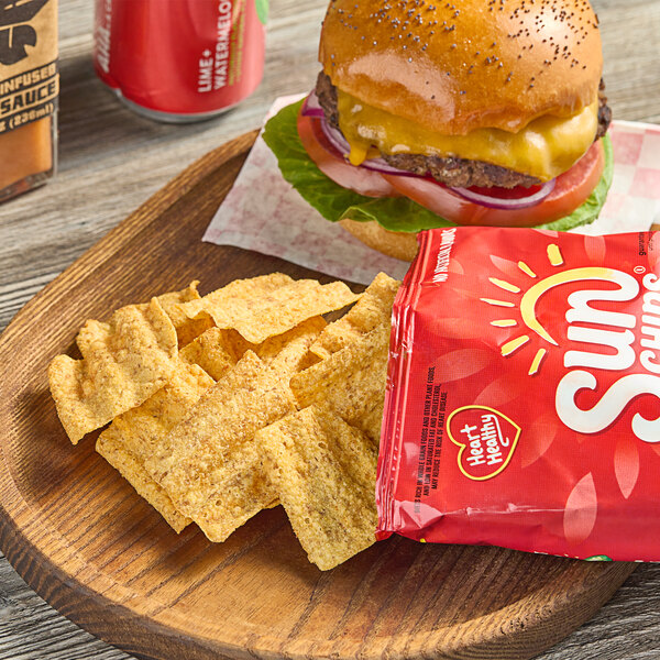 A cheeseburger and a bag of Sun Chips on a wooden plate.