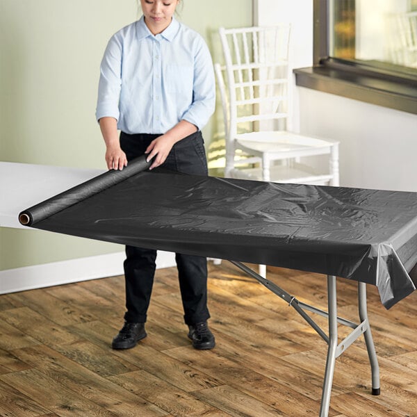 A woman rolling a black plastic sheet on a table.