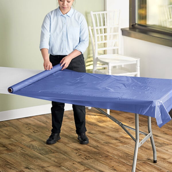 A person rolling a navy blue plastic table cover onto a table.
