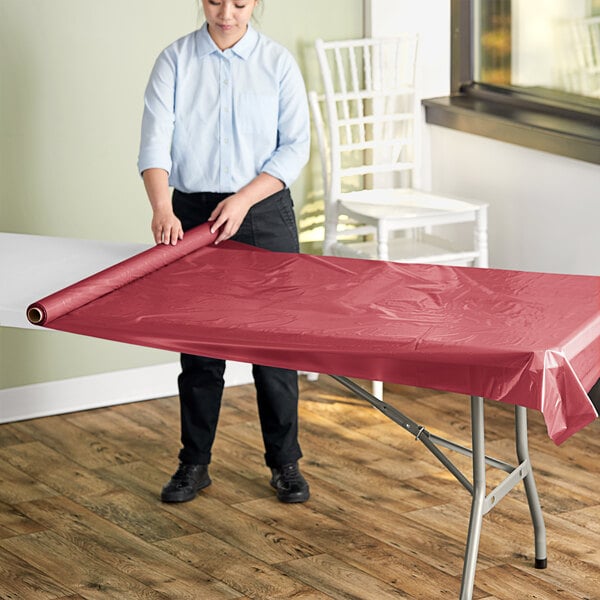 A woman unrolling a red plastic table cover onto an outdoor table.