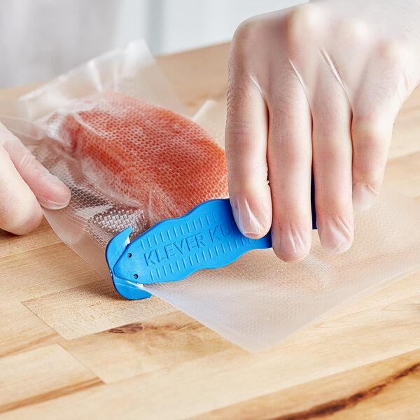 A person using a blue Klever Kutter to cut a plastic bag.