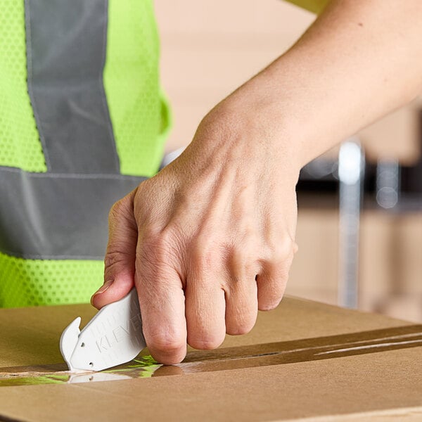A person's hand using a Klever Kutter white safety box cutter to cut a box.