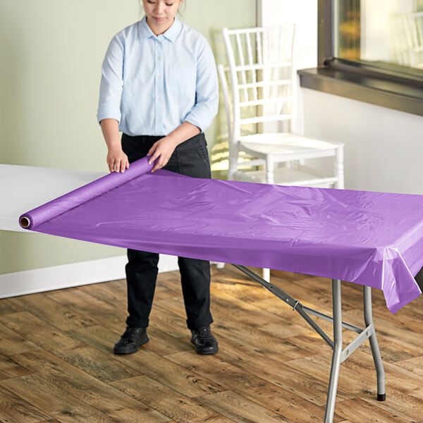 A woman rolling a purple plastic table cover sheet onto a table.