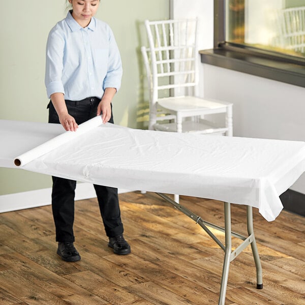 A person rolling a white plastic table cover from a roll.