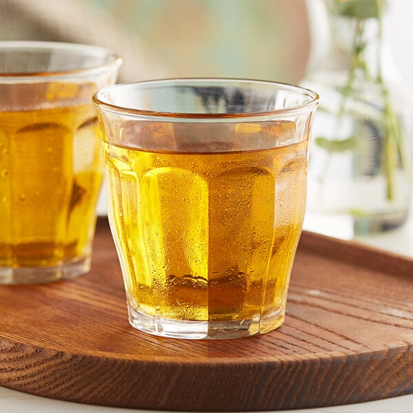 A wooden tray holding two glasses of apple juice.