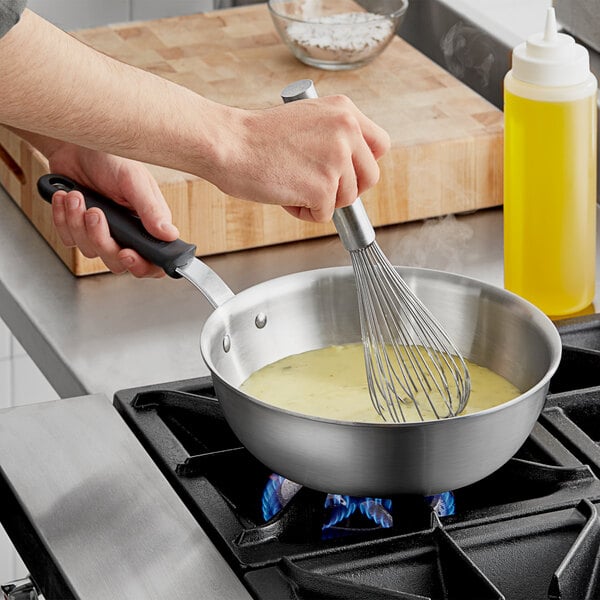 A person stirring food in a Vollrath stainless steel saucier pan with a black handle.