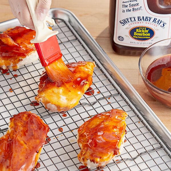 A hand using a sauce brush to put Sweet Baby Ray's Kickin' Bourbon Wing Sauce on chicken