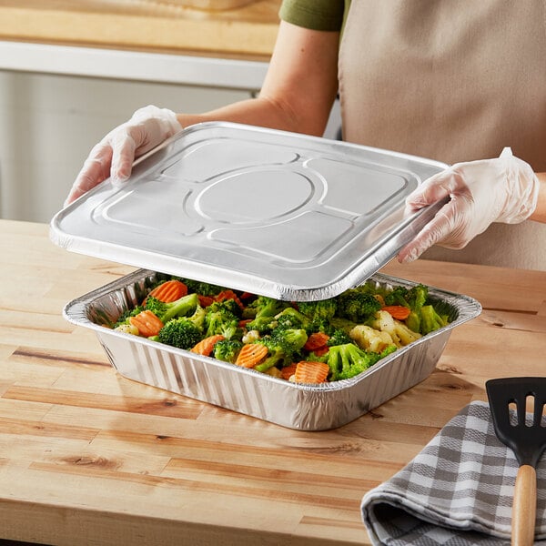 A person holding a Choice foil steam table pan full of food.