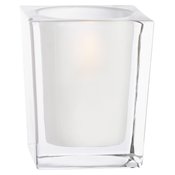 A Sterno frosted clear square glass candle holder with a lit white candle inside.