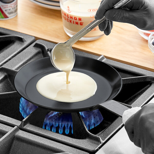 A person pouring liquid into a Matfer Bourgeat carbon steel crepe pan.