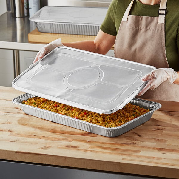 A woman holding a Choice aluminum foil steam table pan full of food.