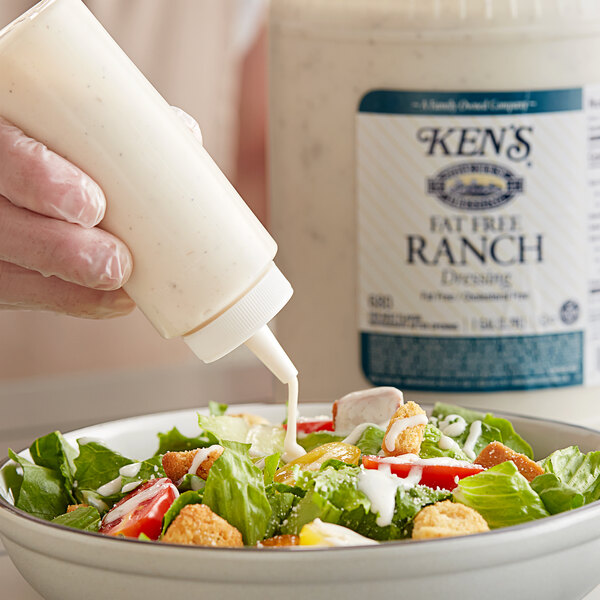 A person pouring Ken's Fat-Free Ranch Dressing onto a salad.