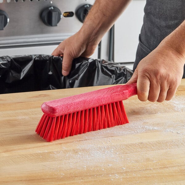 A hand using a red Carlisle counter brush to clean a table.