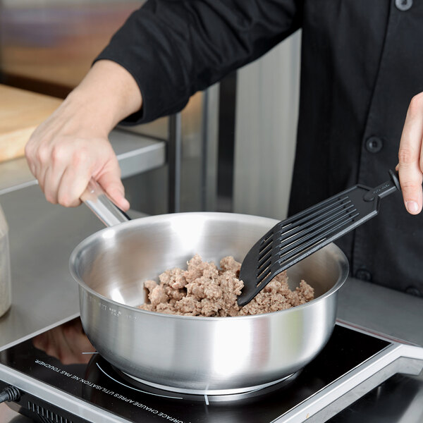 A person cooking food in a Vollrath stainless steel saucier pan.