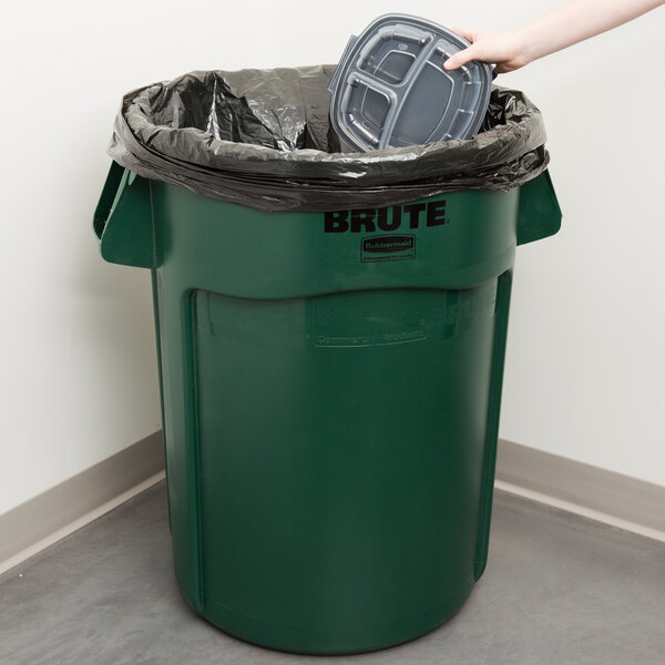 A hand putting a black lid on a green Rubbermaid trash can.