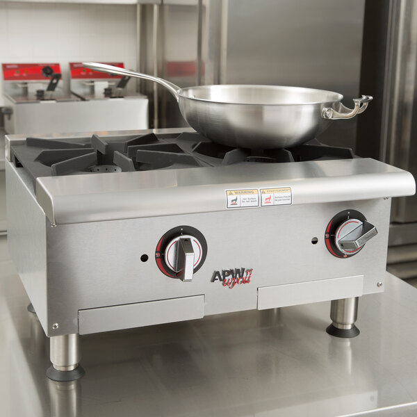 An APW Wyott stainless steel countertop range with pans on top.