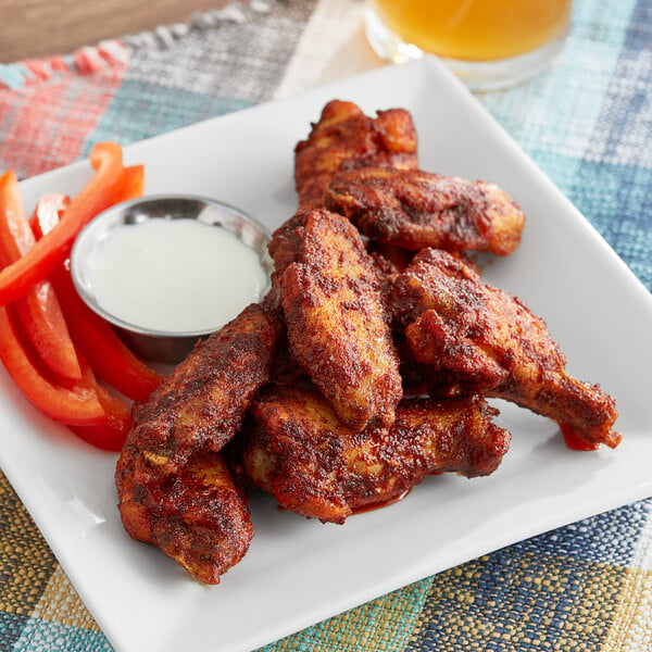 A plate of chicken wings and vegetables with a bowl of white dip.