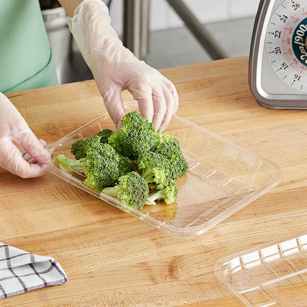 A person in gloves using a plastic tray to hold cut broccoli.