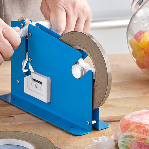 A hand using a blue tape dispenser to seal a plastic bag of candy.