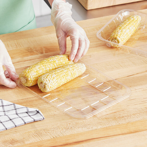 A person in gloves cutting corn on a cutting board.