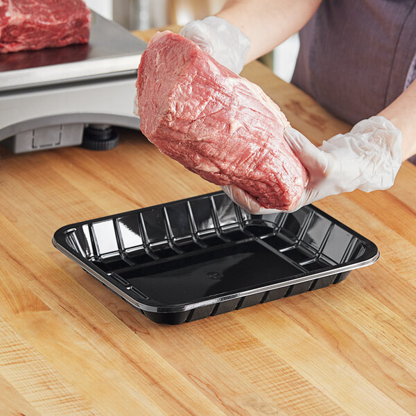 A woman holding a black PET plastic meat tray with a piece of meat inside.