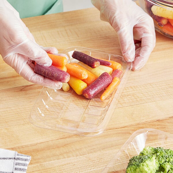 A hand in a plastic glove holding a tray of carrots, broccoli, and sausages.