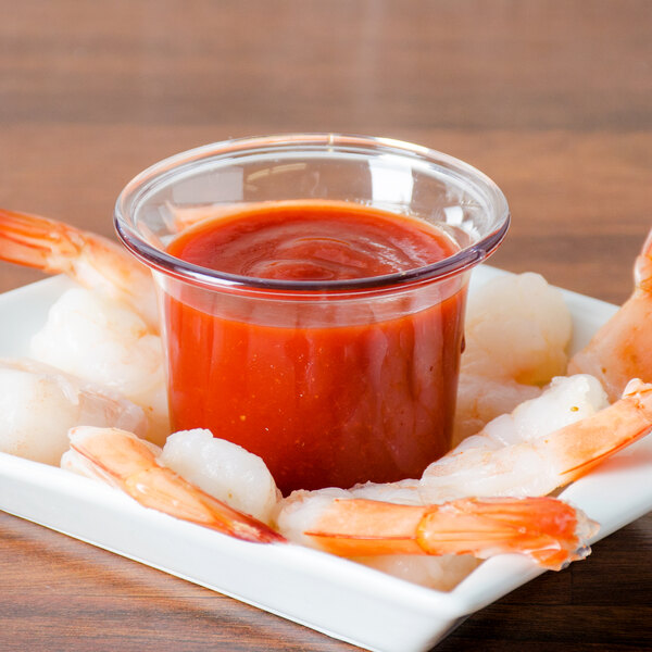A plate of shrimp with Carlisle clear plastic sauce cups filled with red sauce.