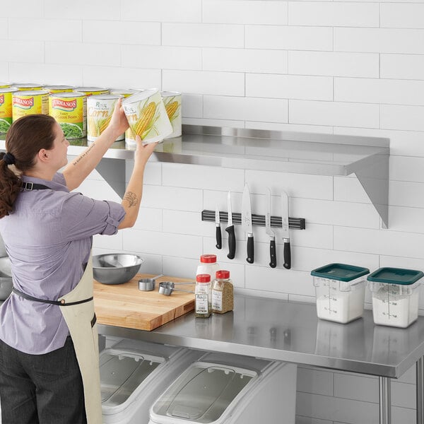A woman in a white apron putting food on a Regency stainless steel wall shelf.