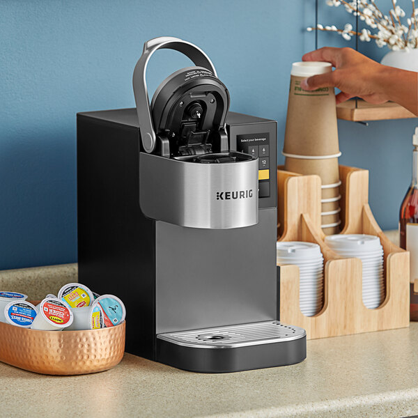 A Keurig K-2500 Plumbed commercial single serve pod coffee maker on a counter with a cup of coffee in it.