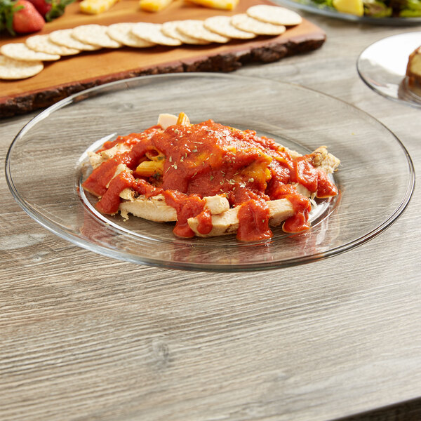 An Anchor Hocking glass platter with pasta and tomato sauce on a table.