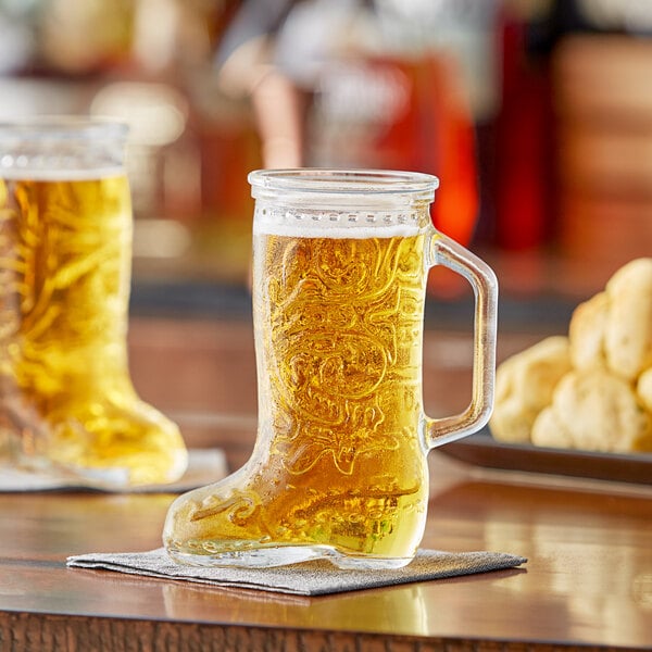 Two Acopa beer glasses with beer in the boot shape.