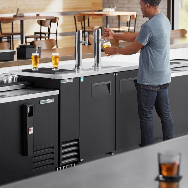 A man pouring beer from a True black kegerator tap.