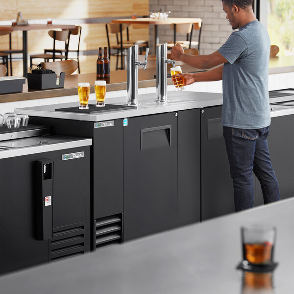 A man pouring beer from a tap on a True kegerator.