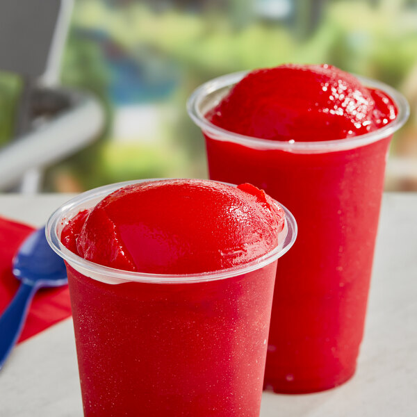 A red frozen dessert in a plastic cup with a blue straw.