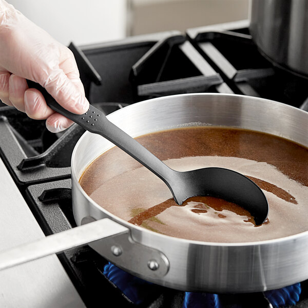 A person stirring a sauce in a pot with a Choice black nylon spoon.