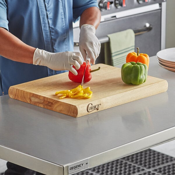 A man cutting red peppers on a Choice wood cutting board on a counter.