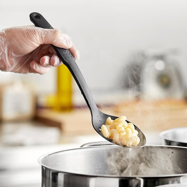 A hand using a Choice black slotted nylon spoon to serve pasta.
