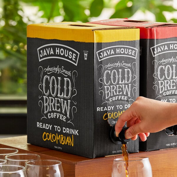 A hand pouring Java House Colombian Cold Brew Coffee from a box into a glass.