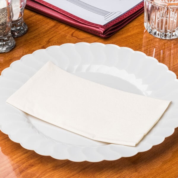 A white plate with a Hoffmaster ivory paper dinner napkin on it.