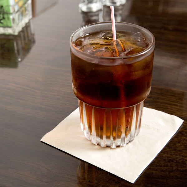 A glass of brown liquid with ice and a Hoffmaster ecru cocktail napkin with a straw.