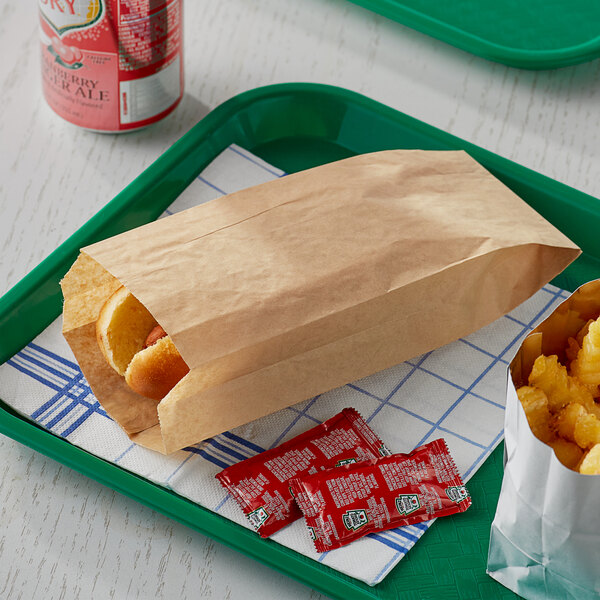 A Bagcraft EcoCraft paper bag with a hot dog in it on a tray with fries.