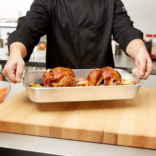 A chef holding a Vollrath aluminum baking and roasting pan full of food.