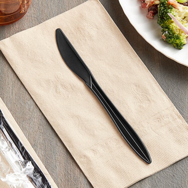 A black Remcoda plastic knife on a napkin next to a plate of food.
