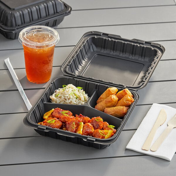 A black Choice plastic container with 3 compartments of food and a drink on a table.